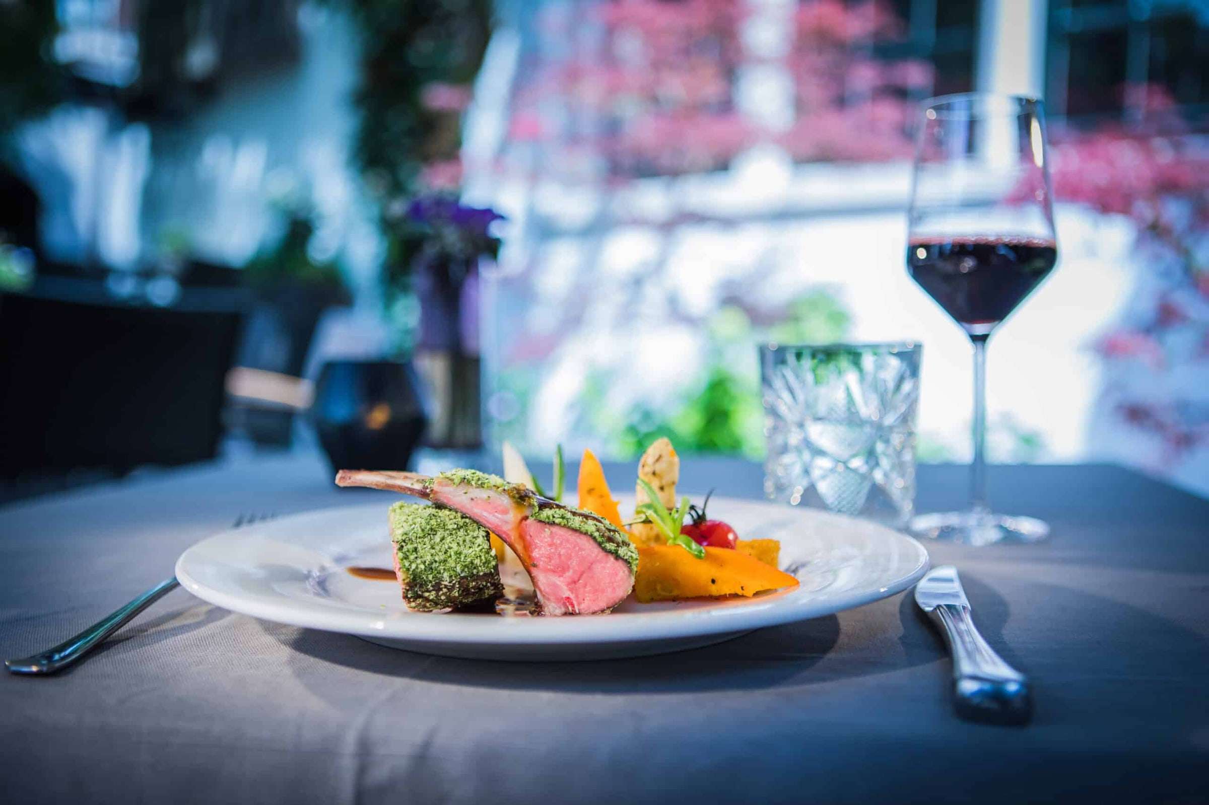 Lamsrack met seizoensgroenten en een glas rode wijn op het terras