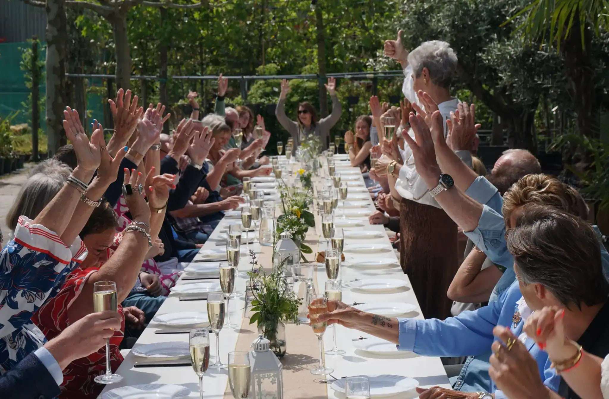 Gasten heffen het glas aan een lange tafel in de tuin