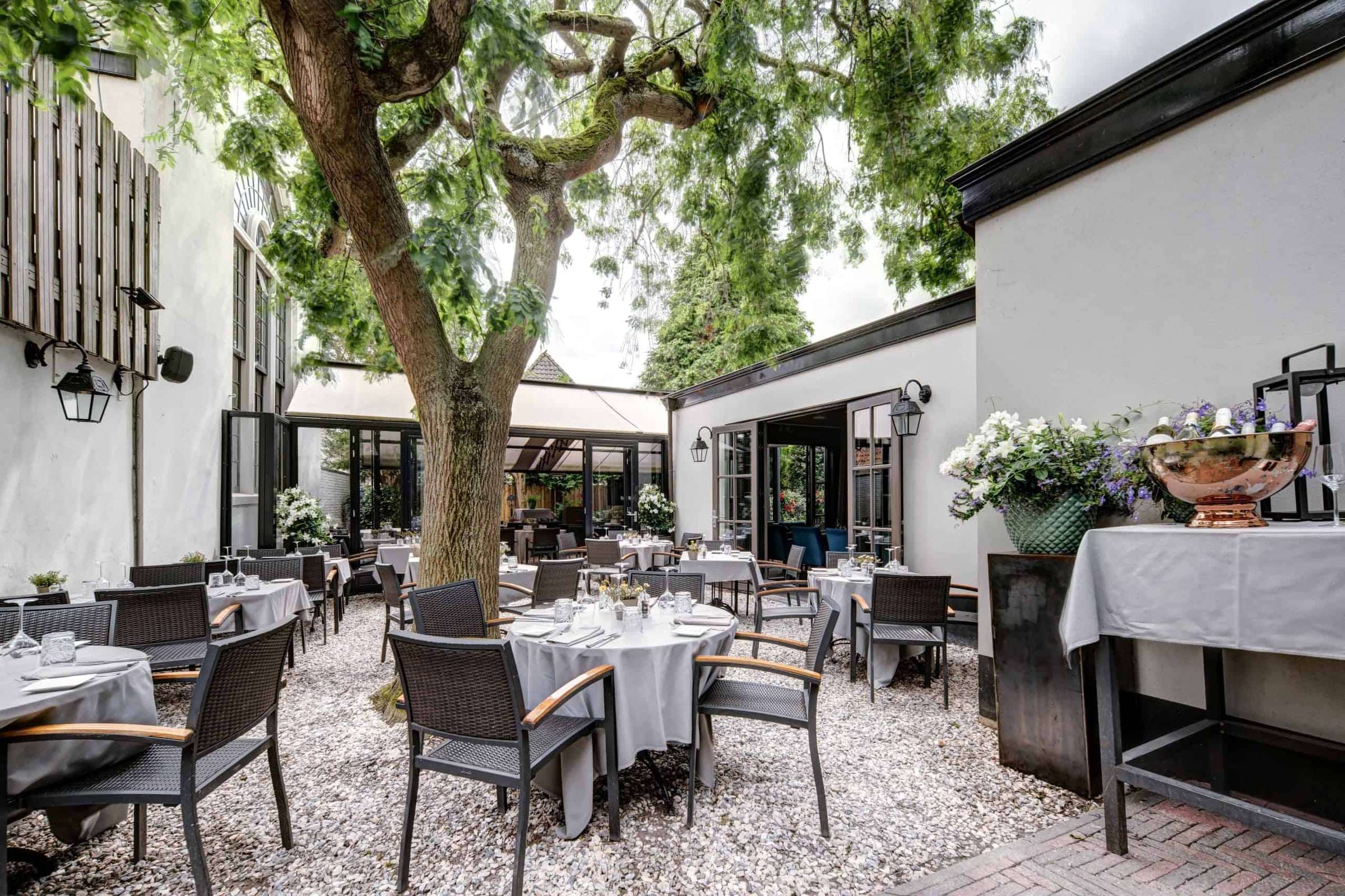Het Heerenterras met gedekte tafels onder een grote boom, tussen witte gevels in het centrum van Montfoort
