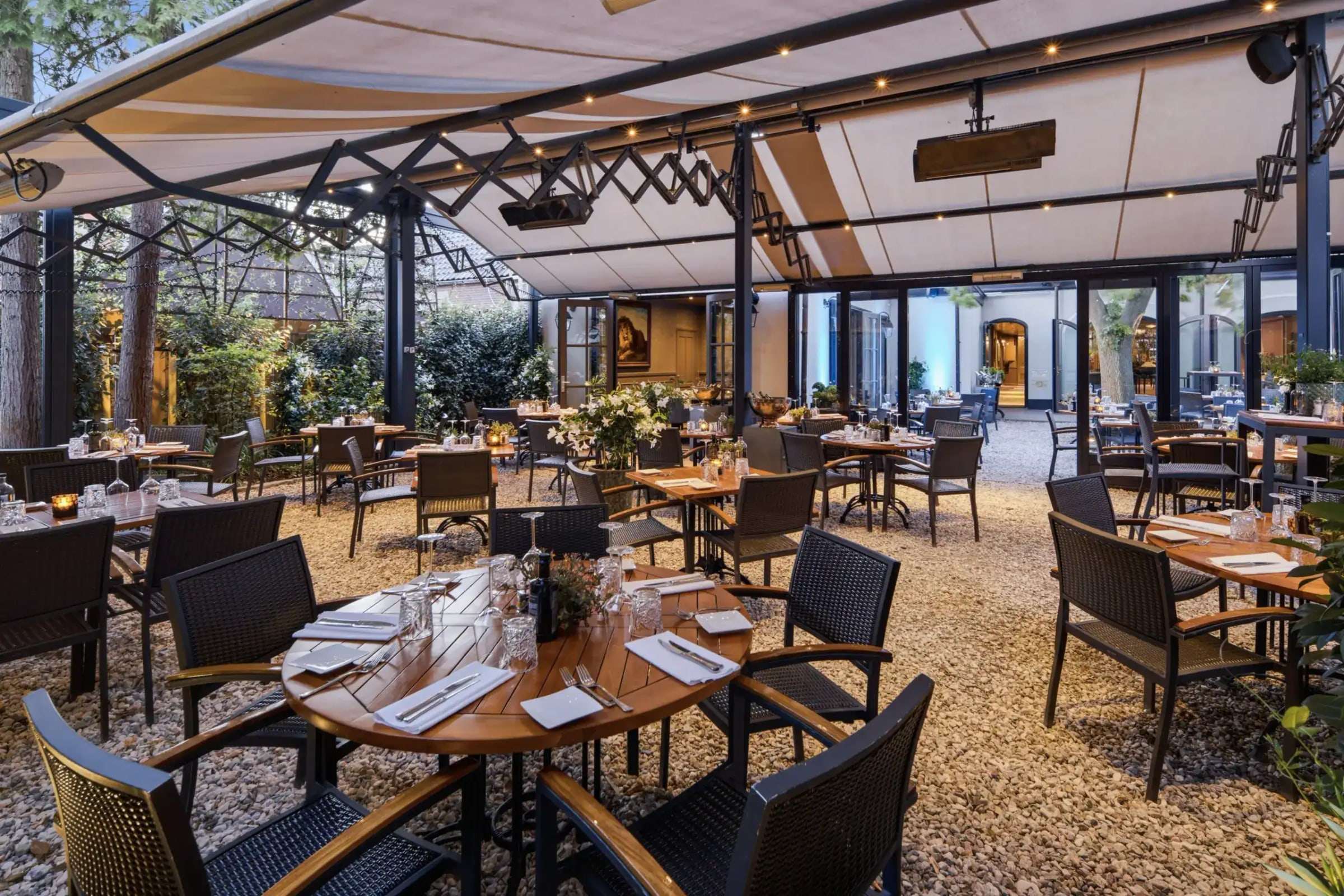 Het overkapte Heerenterras met gedekte tafels in warm avondlicht